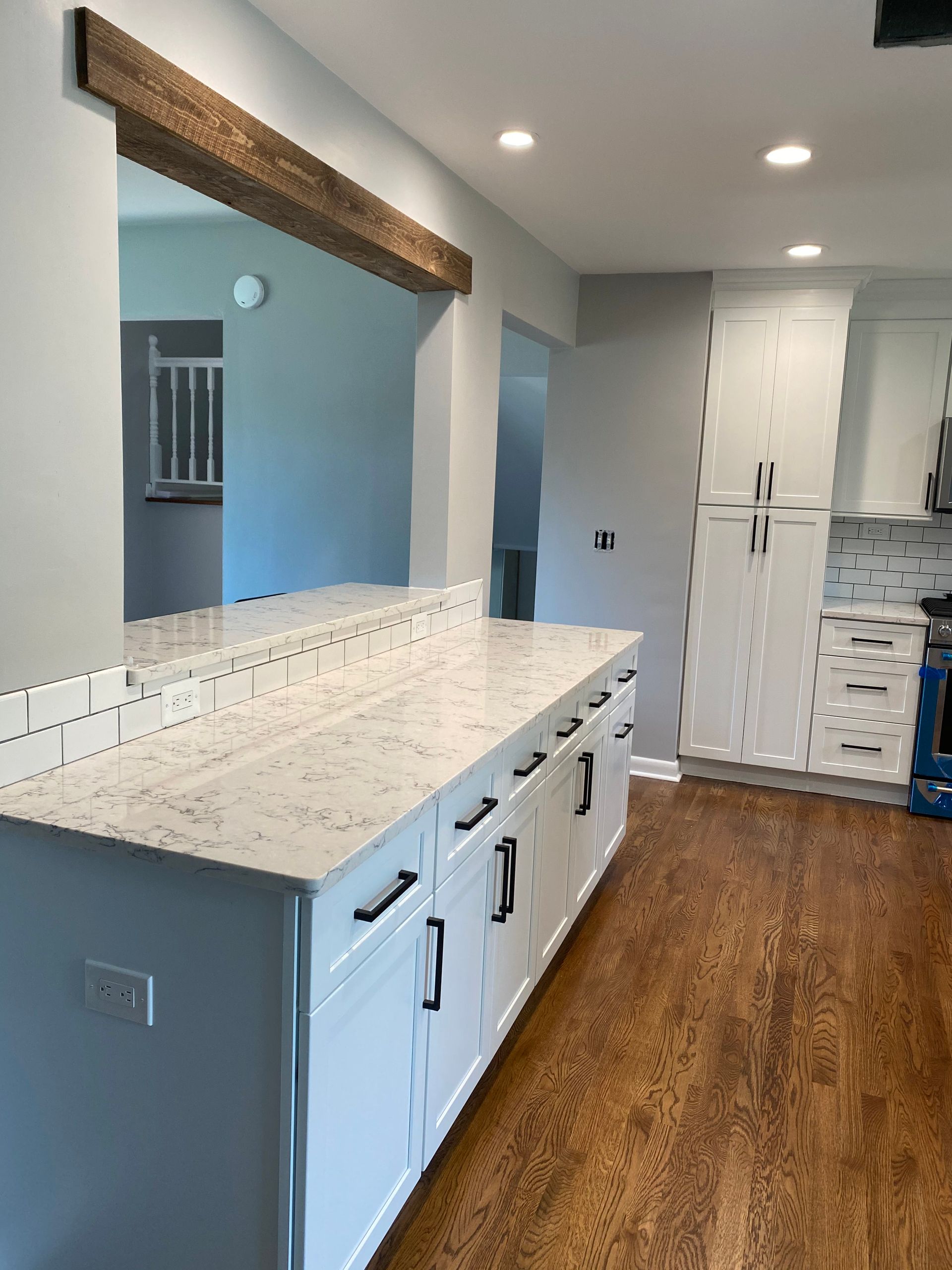 Modern kitchen with white cabinets, granite island, wood beam, and hardwood floors