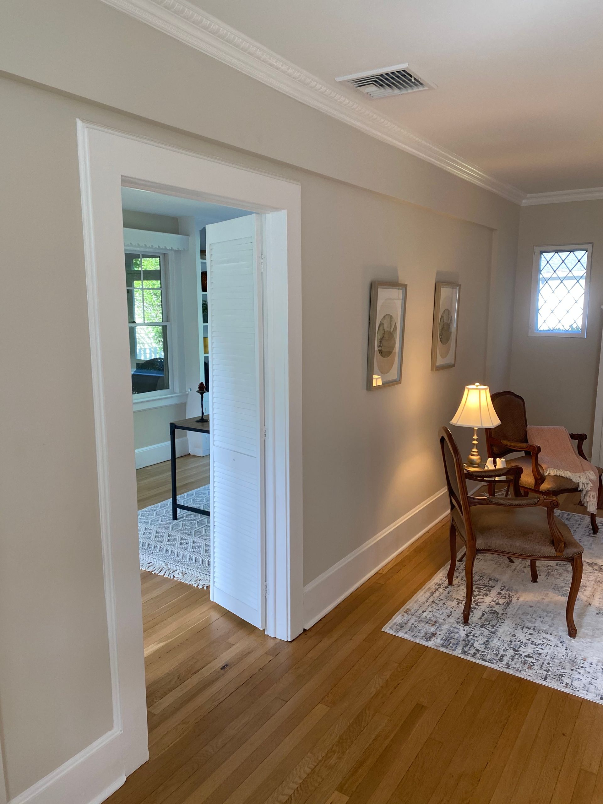 Bright hallway with wood floors, white walls, and a sitting area with a lamp and rug to the right.