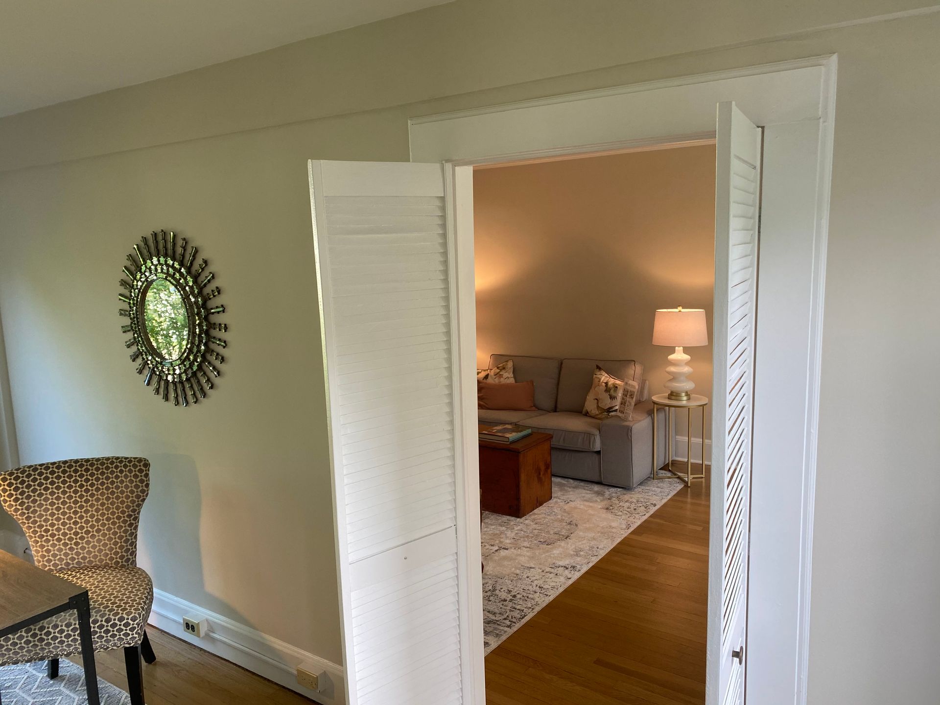 Open white double doors into a softly lit bedroom with a bed, lamp, rug, and armchair.
