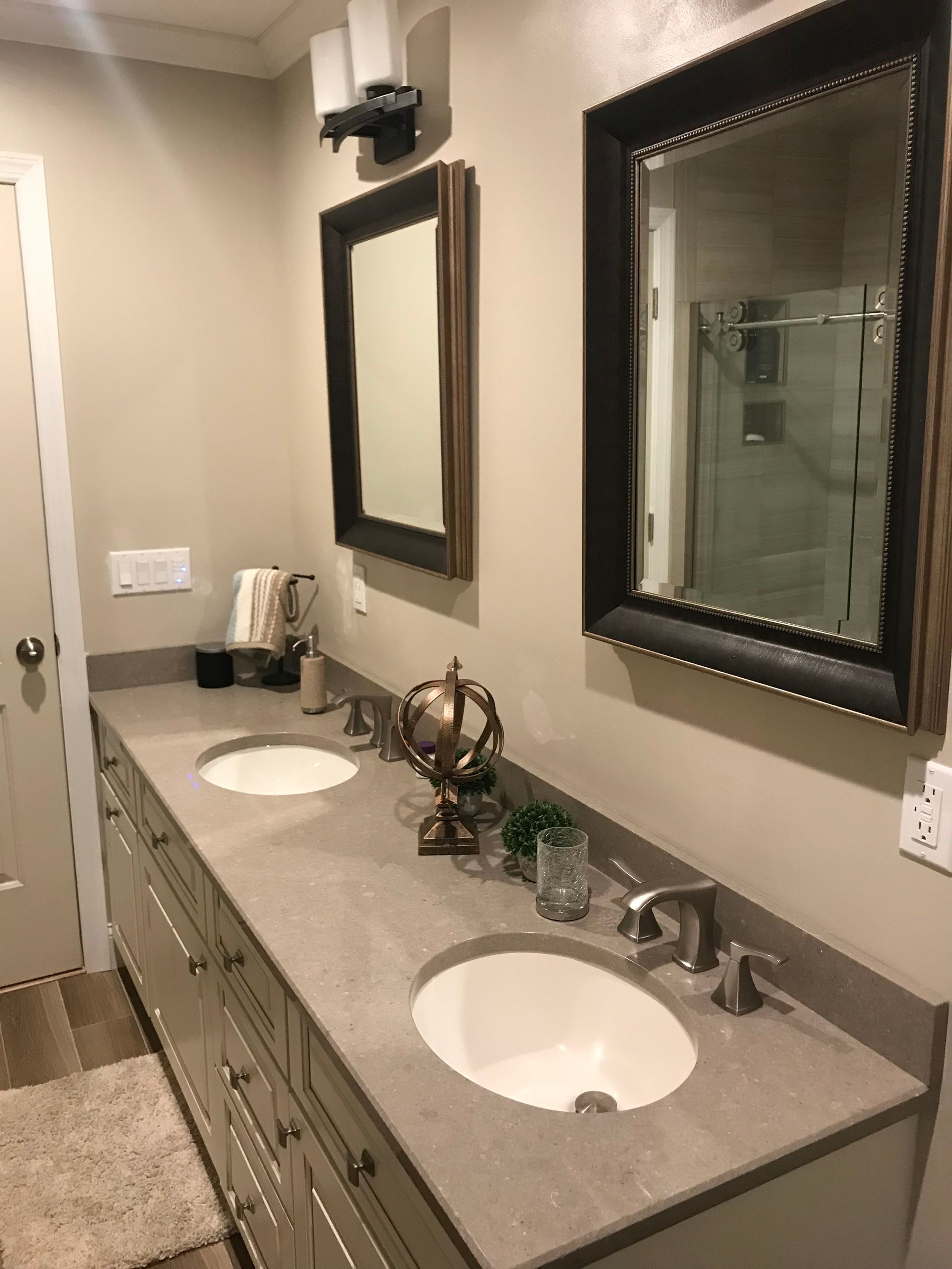 Bathroom vanity with two sinks, mirrors, and countertop accessories in a beige tiled room