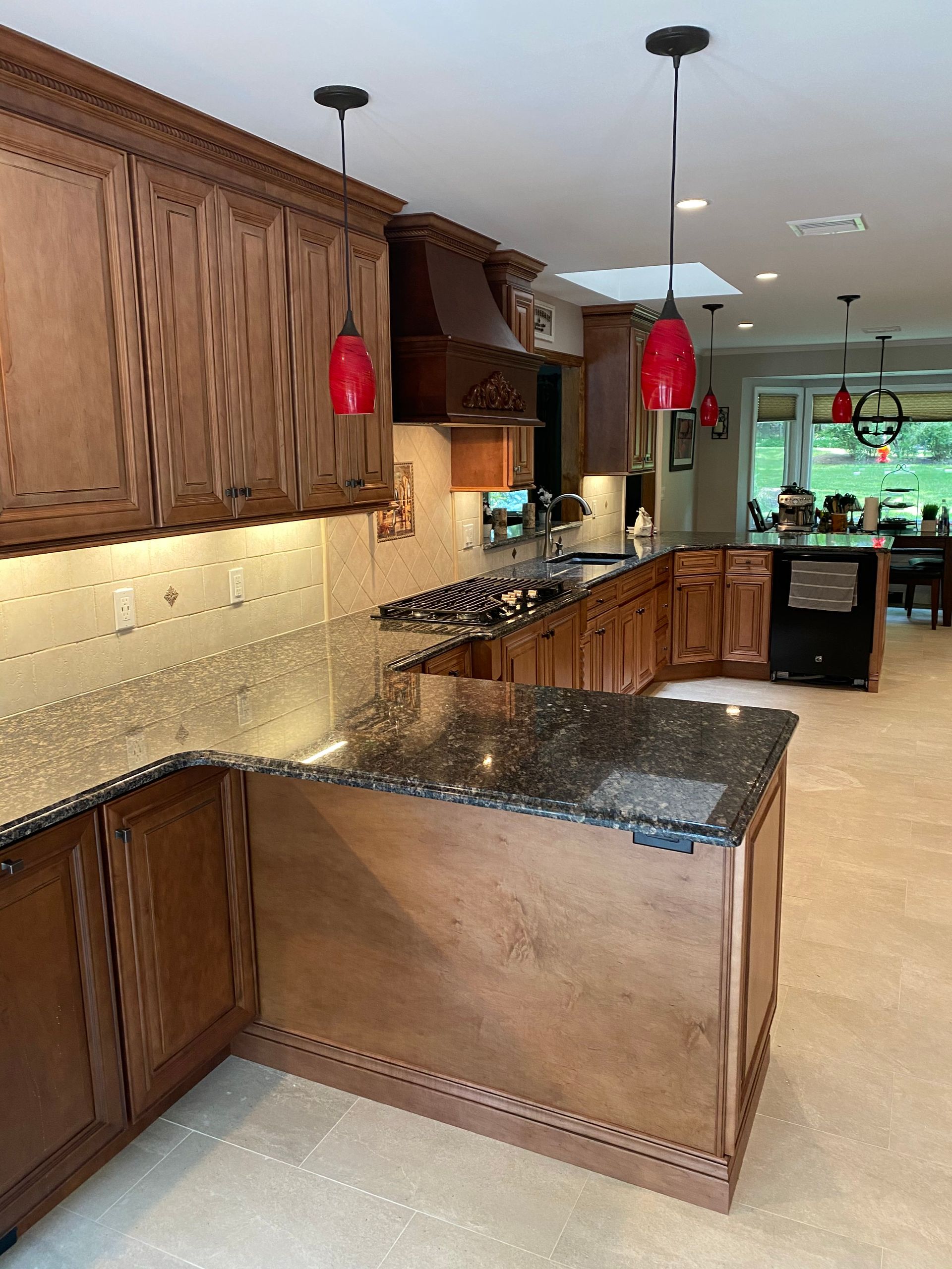 Kitchen with wooden cabinets, granite island, red pendant lights, and a view into a bright dining area