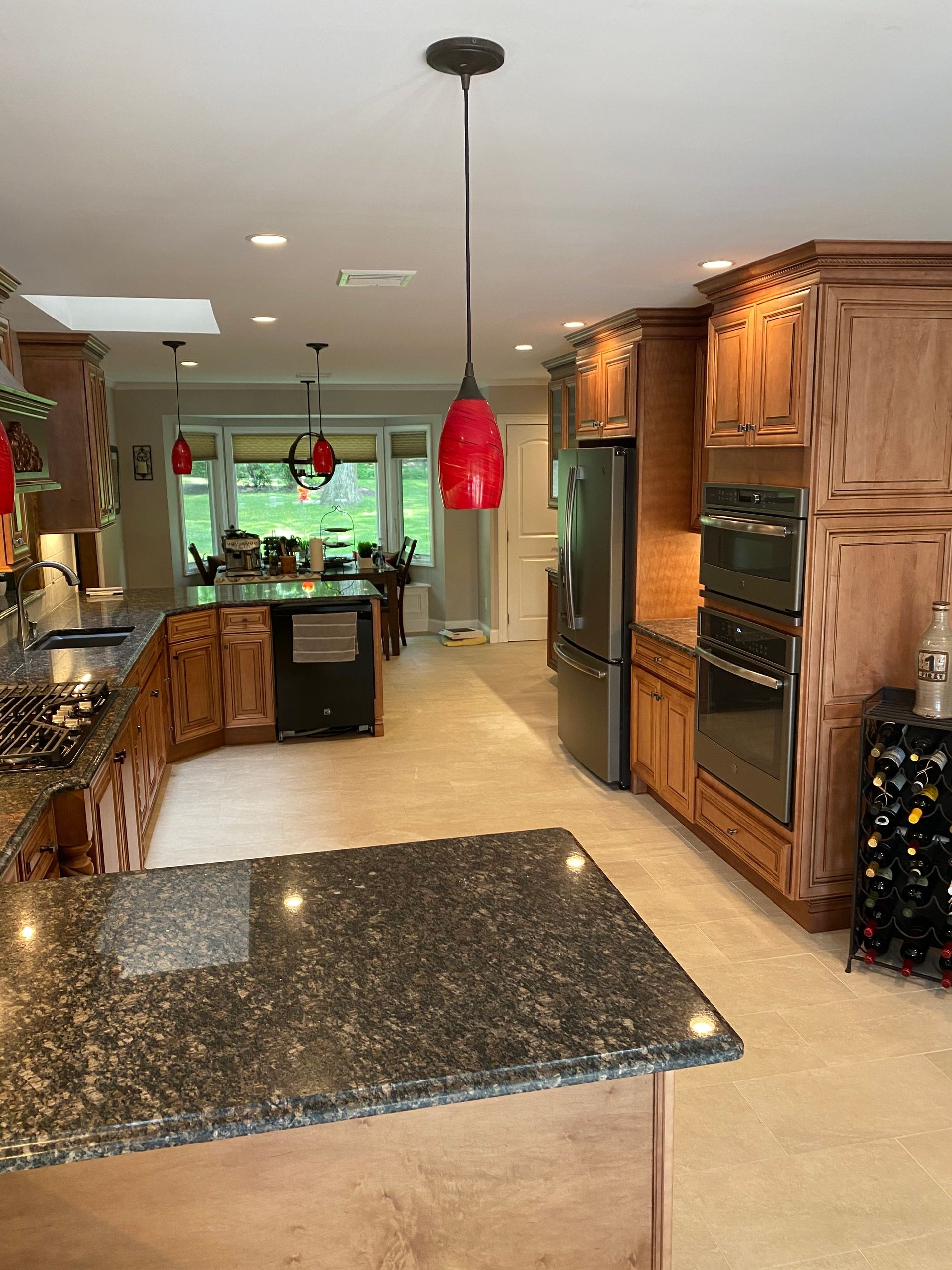 Kitchen interior with black granite island, wood cabinets, red pendant lights, and a view to a bright dining area.