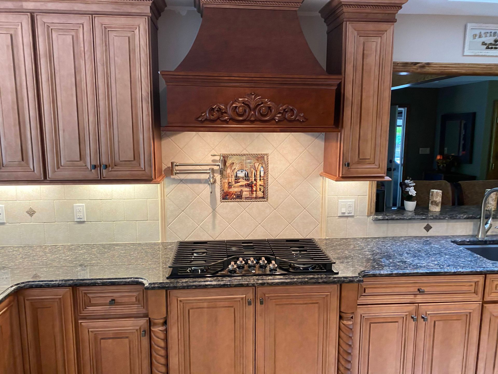 Wooden kitchen with granite countertops, gas range, decorative hood, and beige tile backsplash