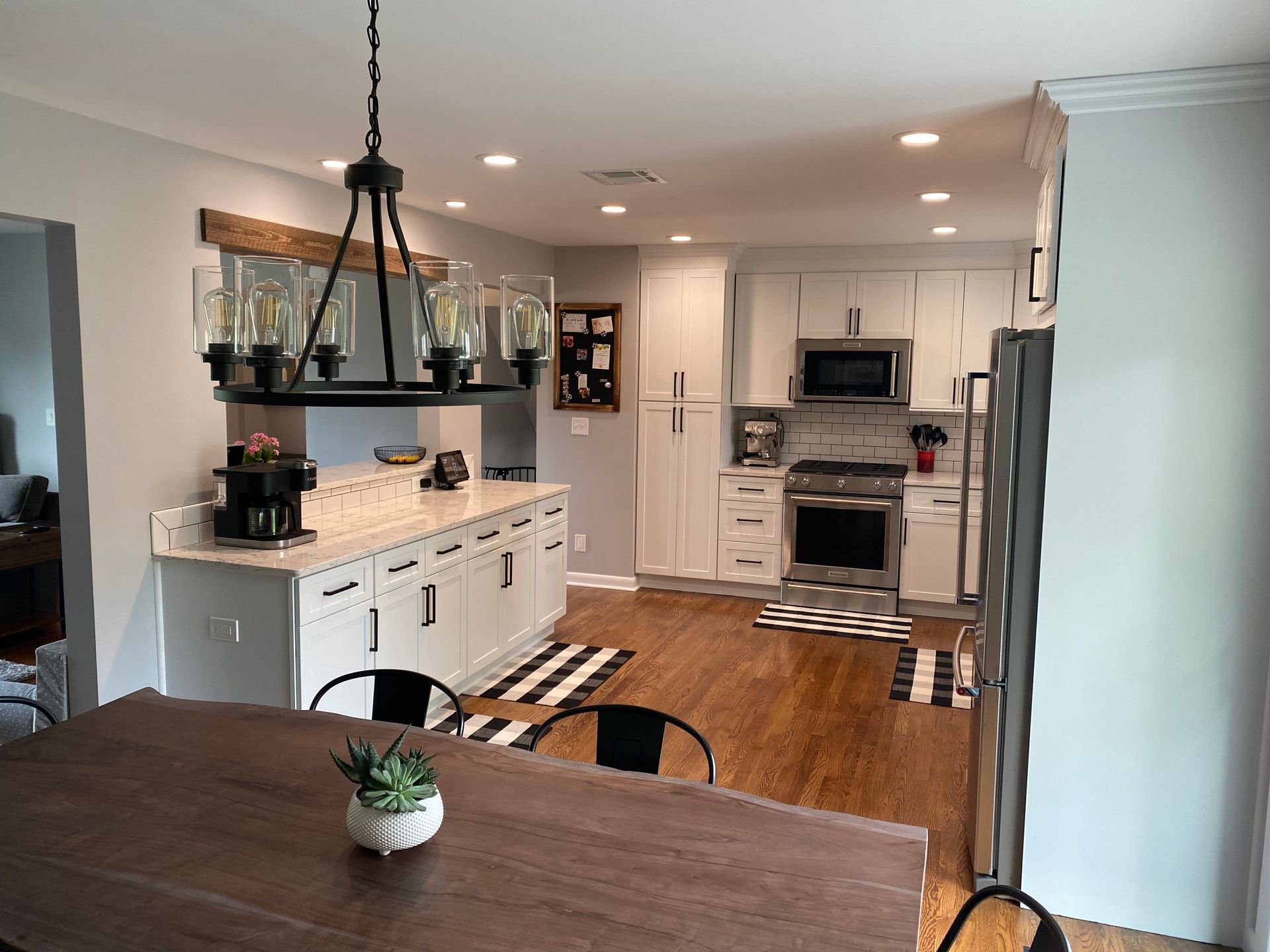 Bright modern kitchen with white cabinets, wood island table, and black pendant lights