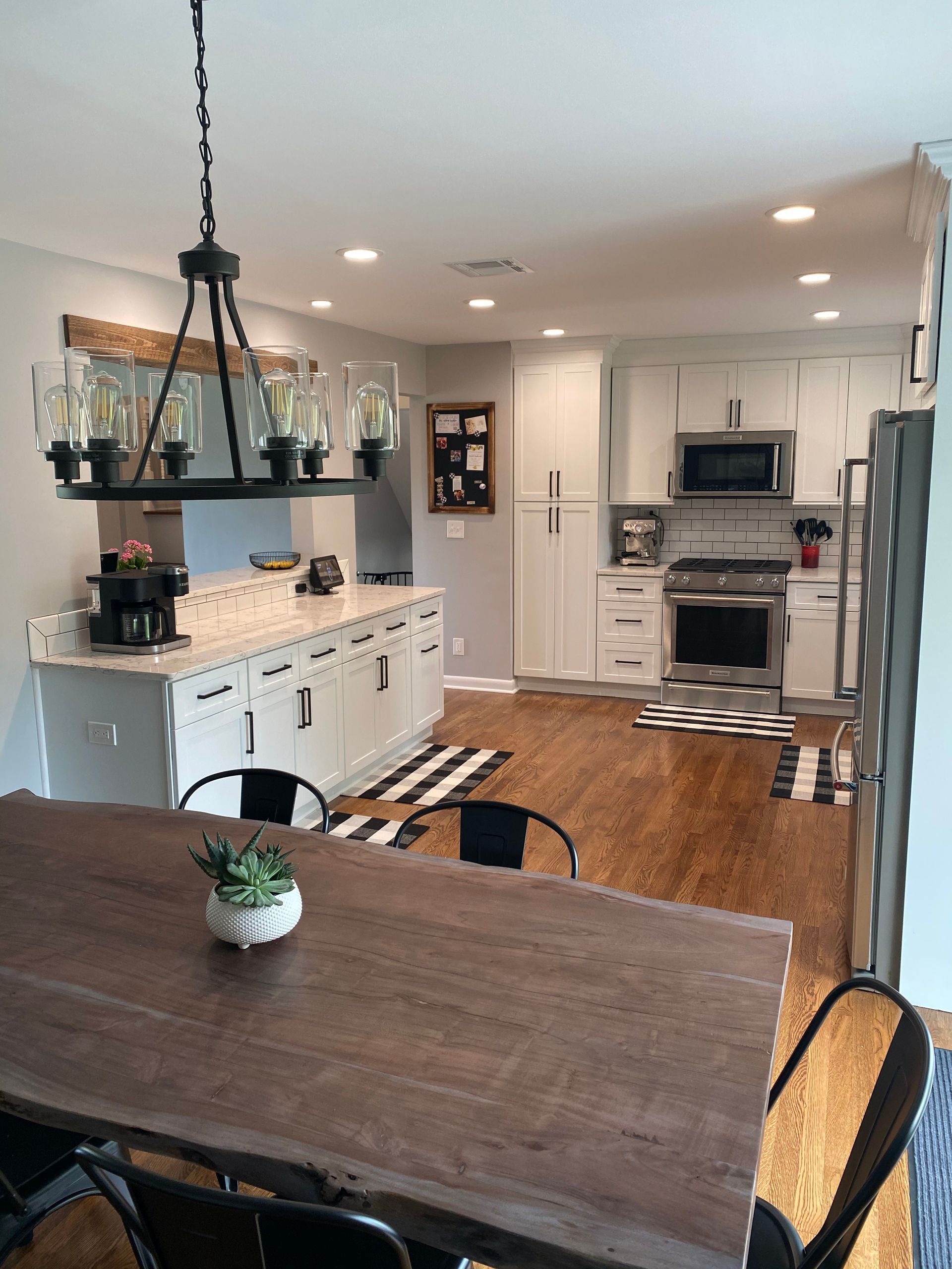 Bright modern kitchen and dining area with wooden table, white cabinets, pendant light, and hardwood floors