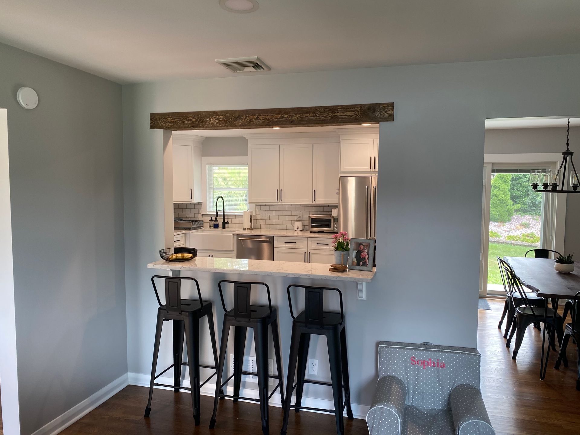 Kitchen pass-through with three black stools, gray walls, and a dining room visible beyond