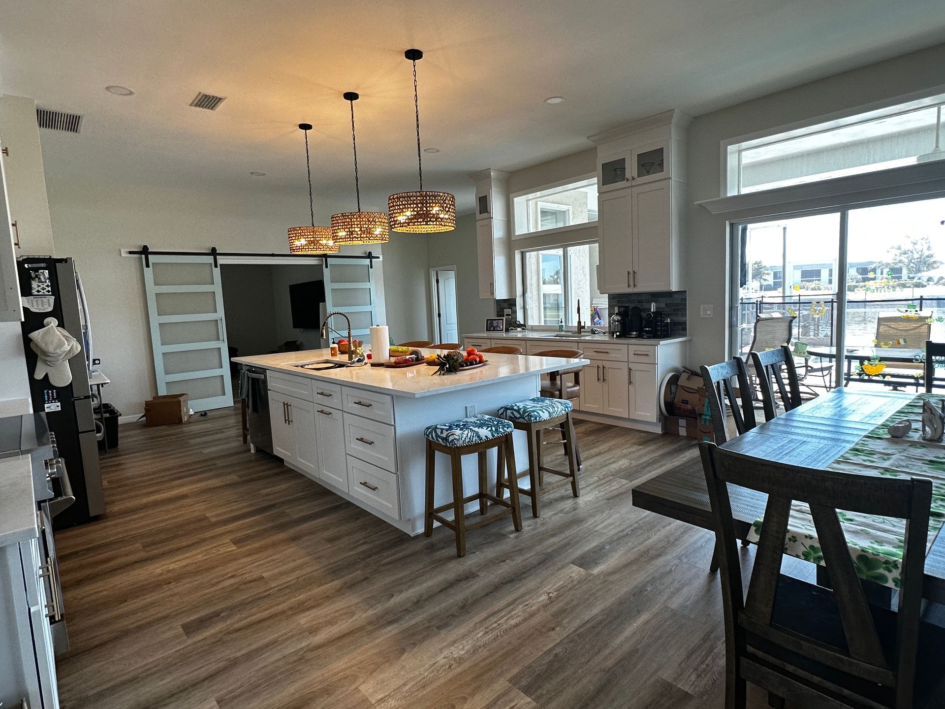Bright modern kitchen with a large island, wood floors, pendant lights, and dining table near sliding glass doors