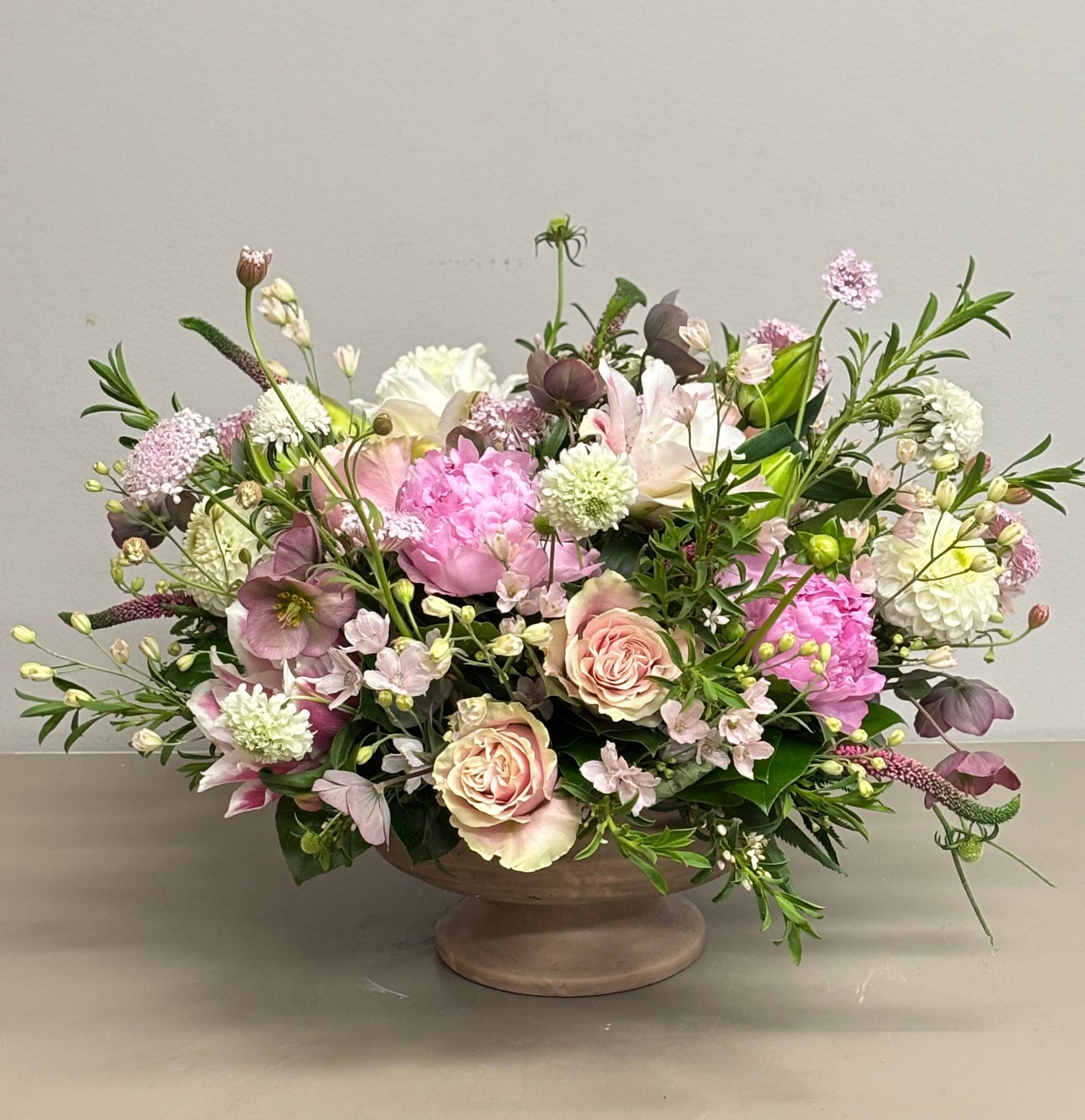 A floral arrangement in a brown vase. The arrangement features pink, white, and green flowers.