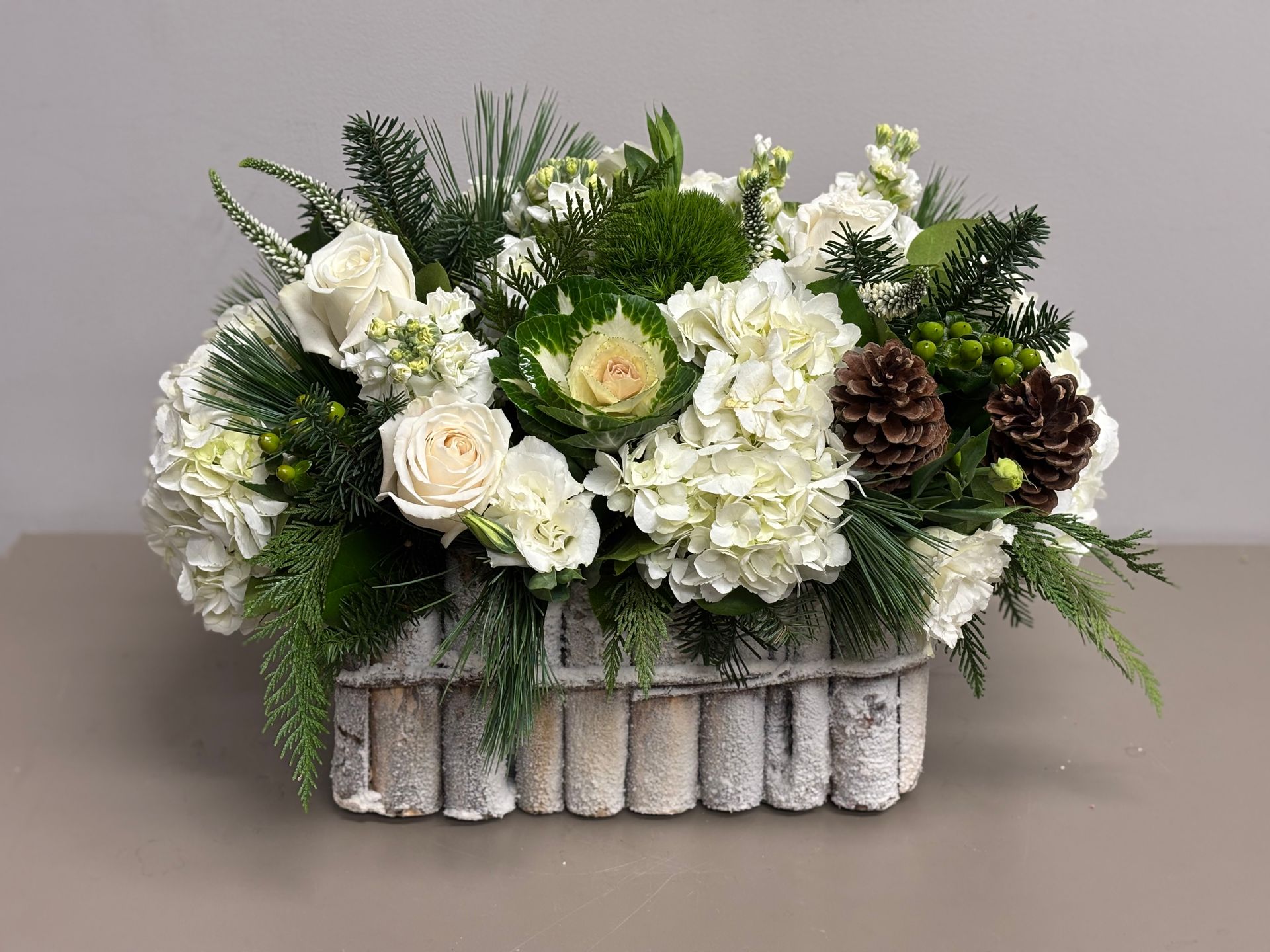 White floral arrangement with pinecones and greenery in a birch-bark-style container