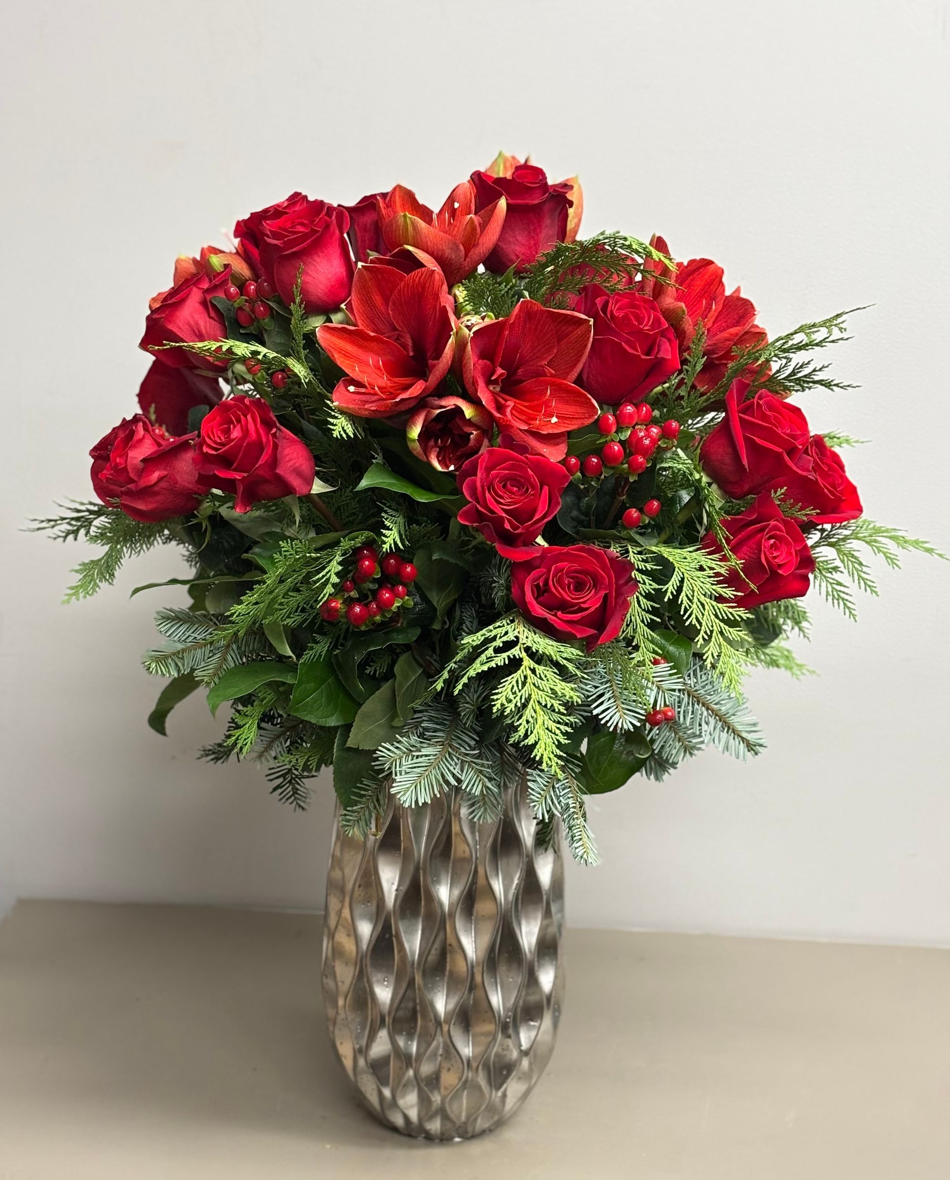 Red roses, tulips, and berries in a silver vase, a festive floral arrangement