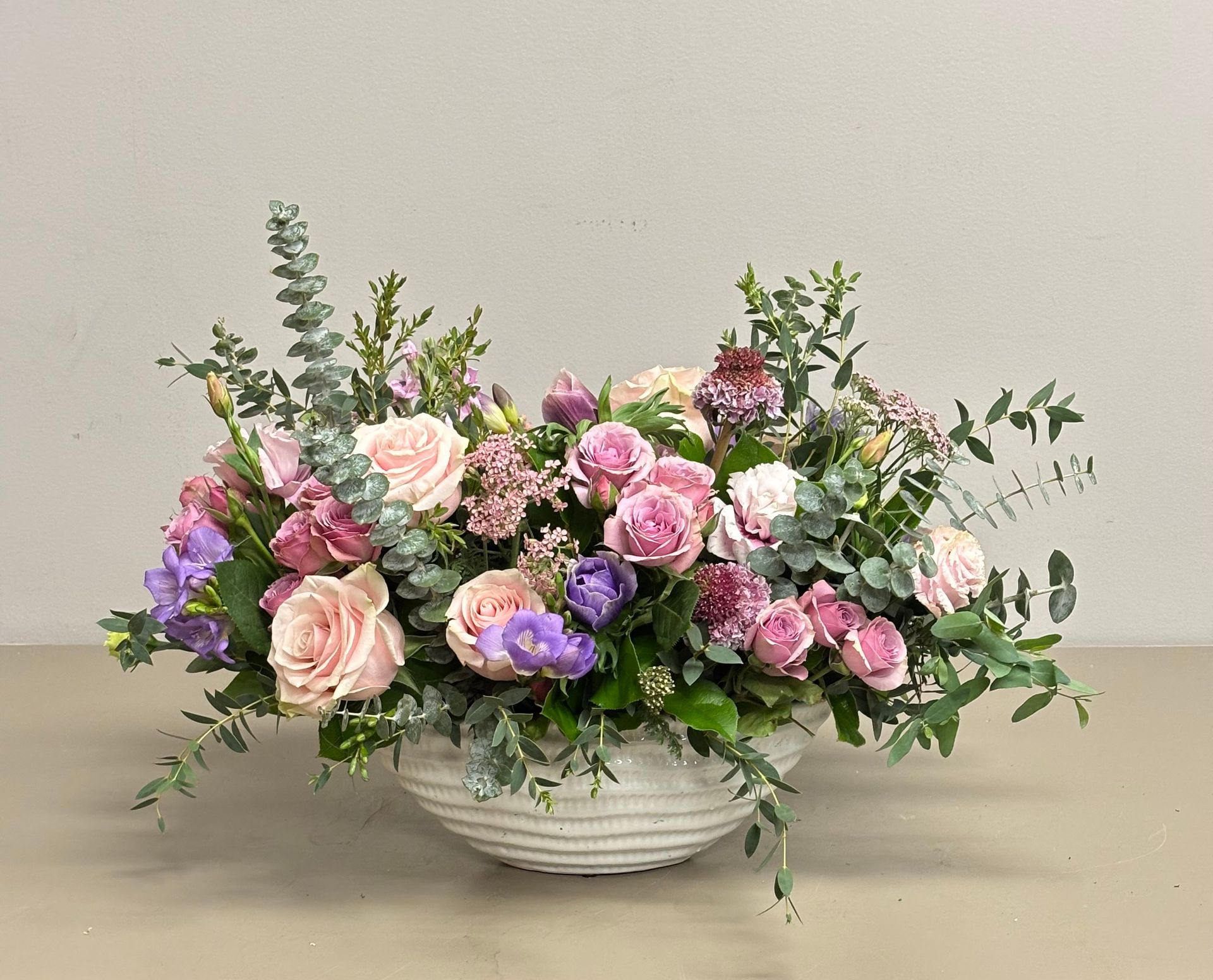 Floral arrangement with pink and purple roses, nestled in a white, textured bowl with greenery