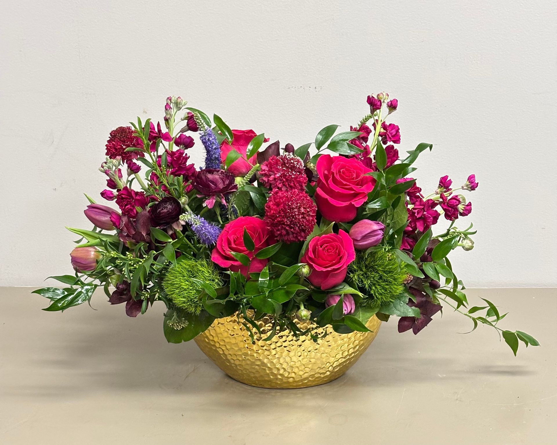 Floral arrangement in a gold textured bowl, featuring pink and purple blooms with greenery