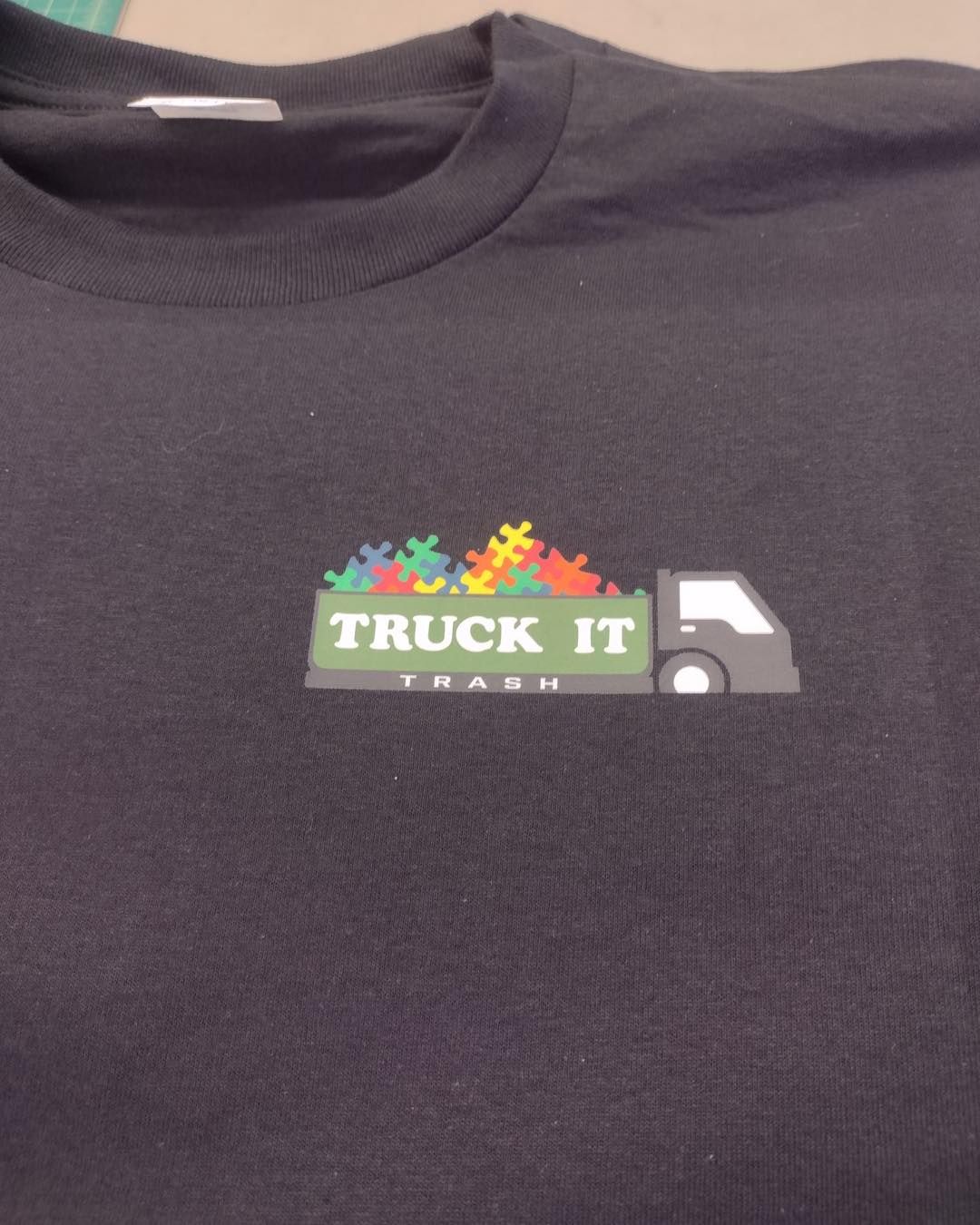 Black t-shirt with a truck graphic carrying colorful puzzle pieces. Text says 