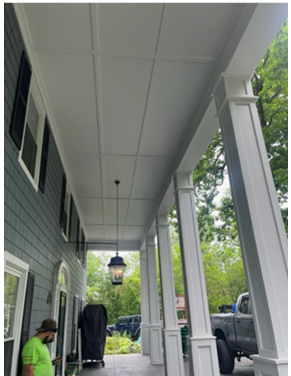 A man in a green shirt is standing on the porch of a house