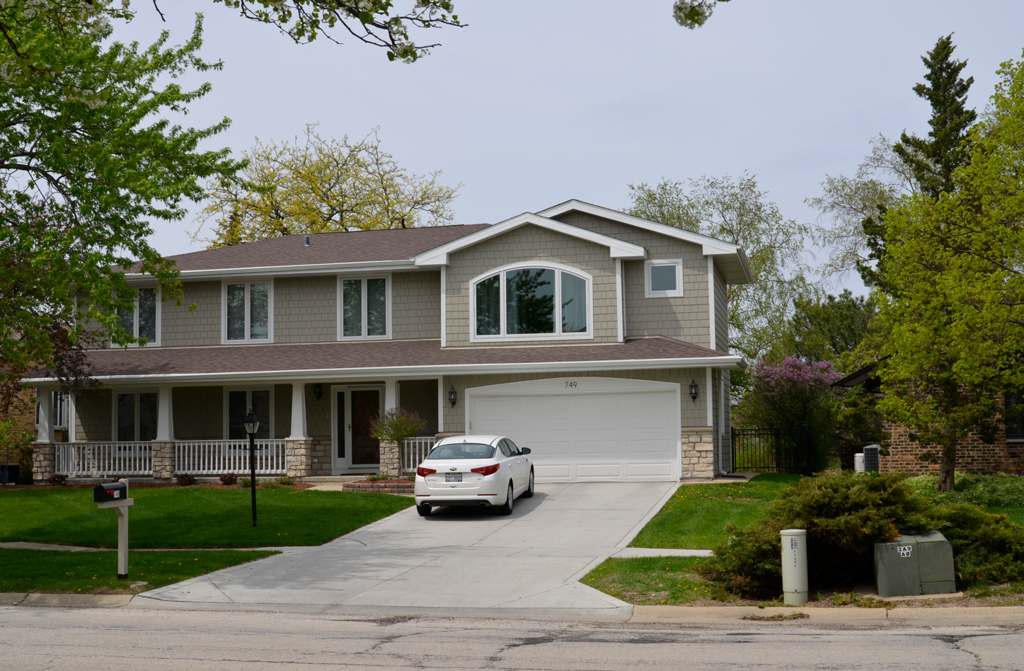 A white car is parked in front of a large house