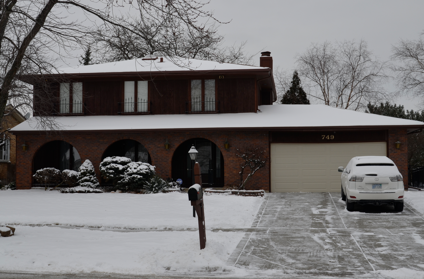 A white car is parked in front of a snow covered house
