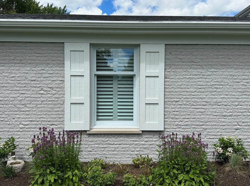 A white brick house with a window and white shutters