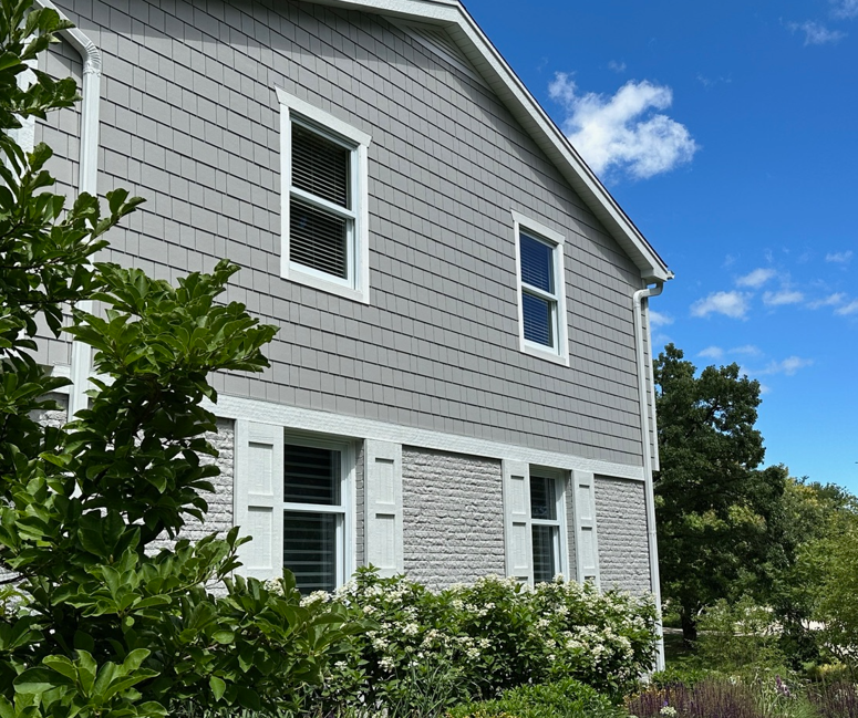 A gray house with white shutters and a blue sky in the background
