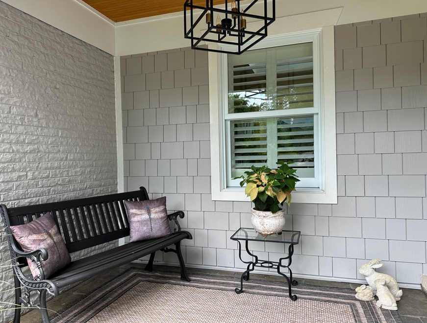 A porch with a bench and a window with shutters