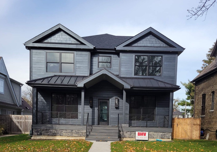 Two-story gray house with black accents, covered porch, and front steps on a grassy lawn.