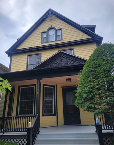 A yellow house with a black porch and stairs