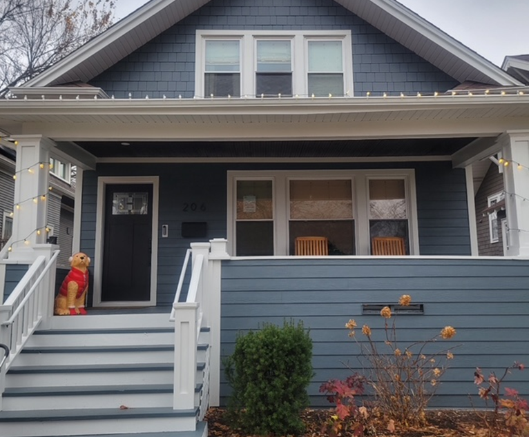 Blue house with white trim, porch, steps, and a dog statue.