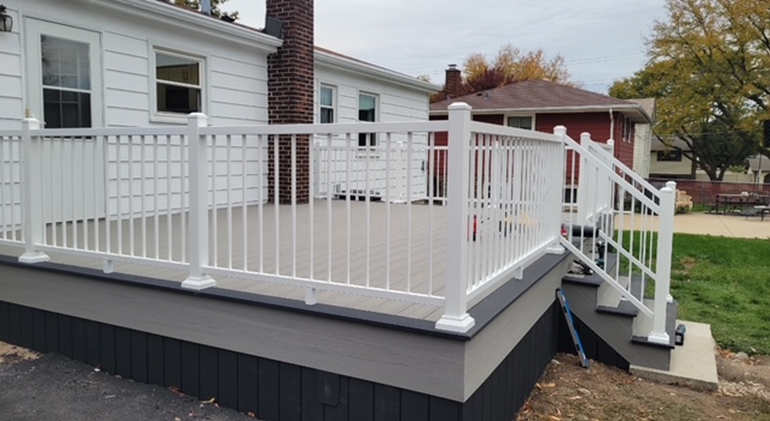 White railing on a composite deck attached to a white house with a chimney and a nearby house.
