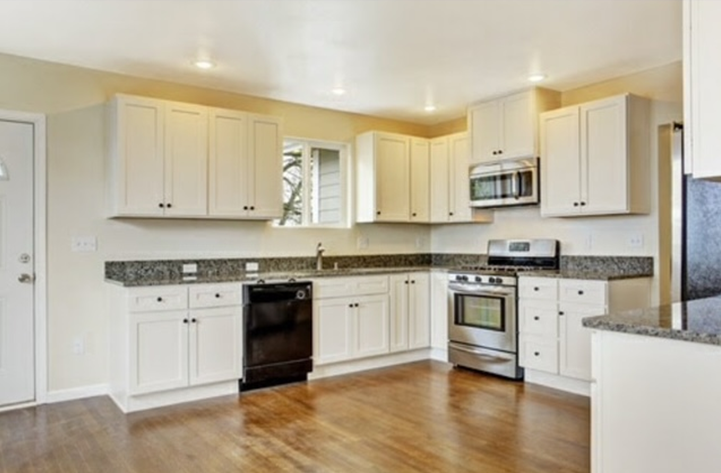 Cream kitchen with white cabinets, dark appliances, granite countertops, and wood floor.