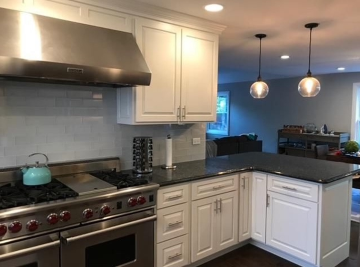Modern white kitchen with stainless steel appliances, dark countertop, and pendant lights.