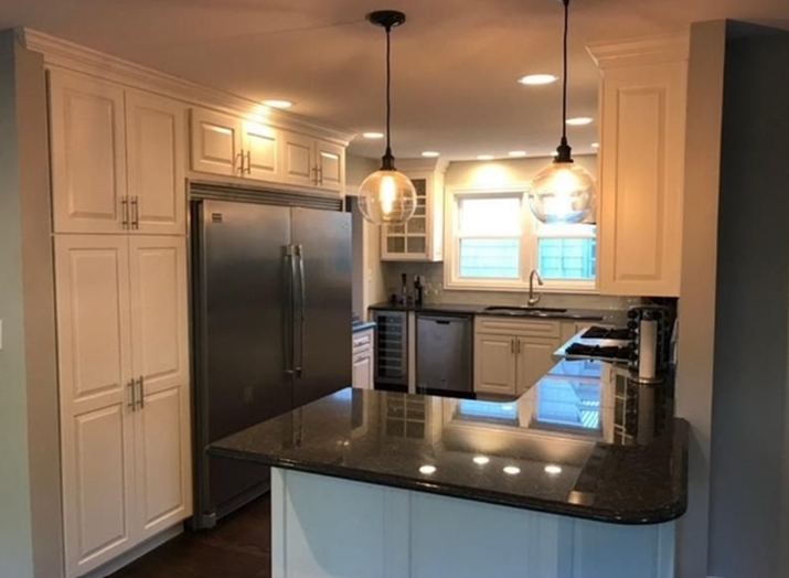 A modern kitchen with white cabinets, stainless steel appliances, a dark countertop, and pendant lights.