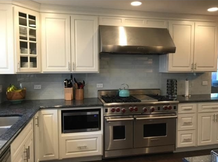 White kitchen with stainless steel appliances, dark countertops, and light blue tile backsplash.