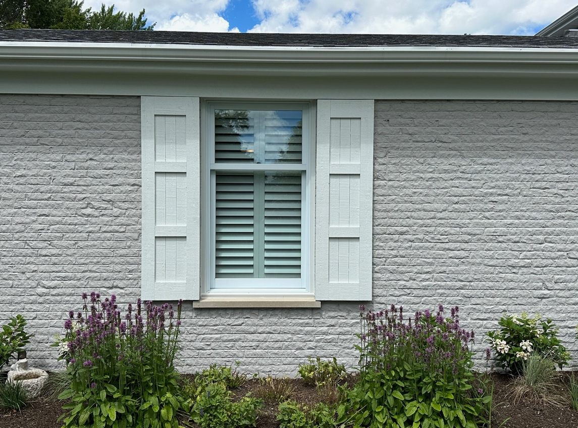 A white brick house with a window and white shutters.