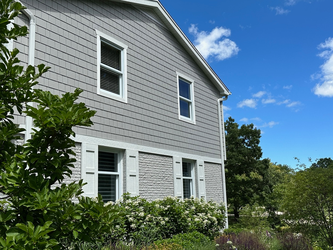 A gray house with white shutters and a blue sky in the background.