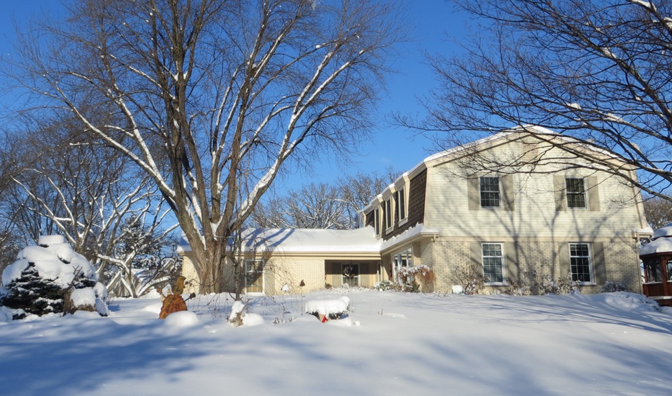 A large white house is surrounded by snow and trees.
