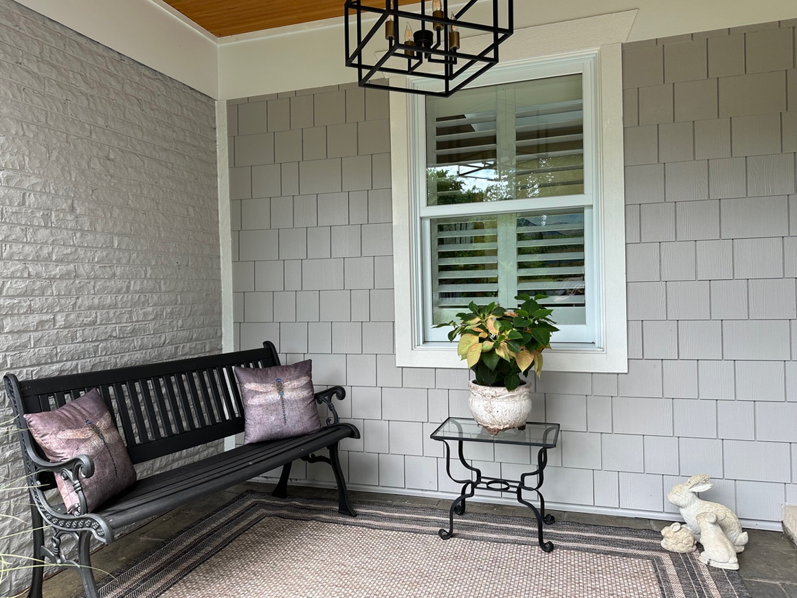 A porch with a bench , table , vase of flowers and a window.