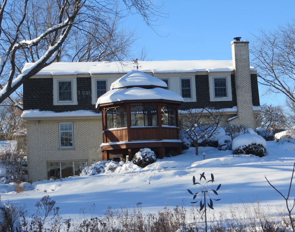 A house with a gazebo in front of it covered in snow.