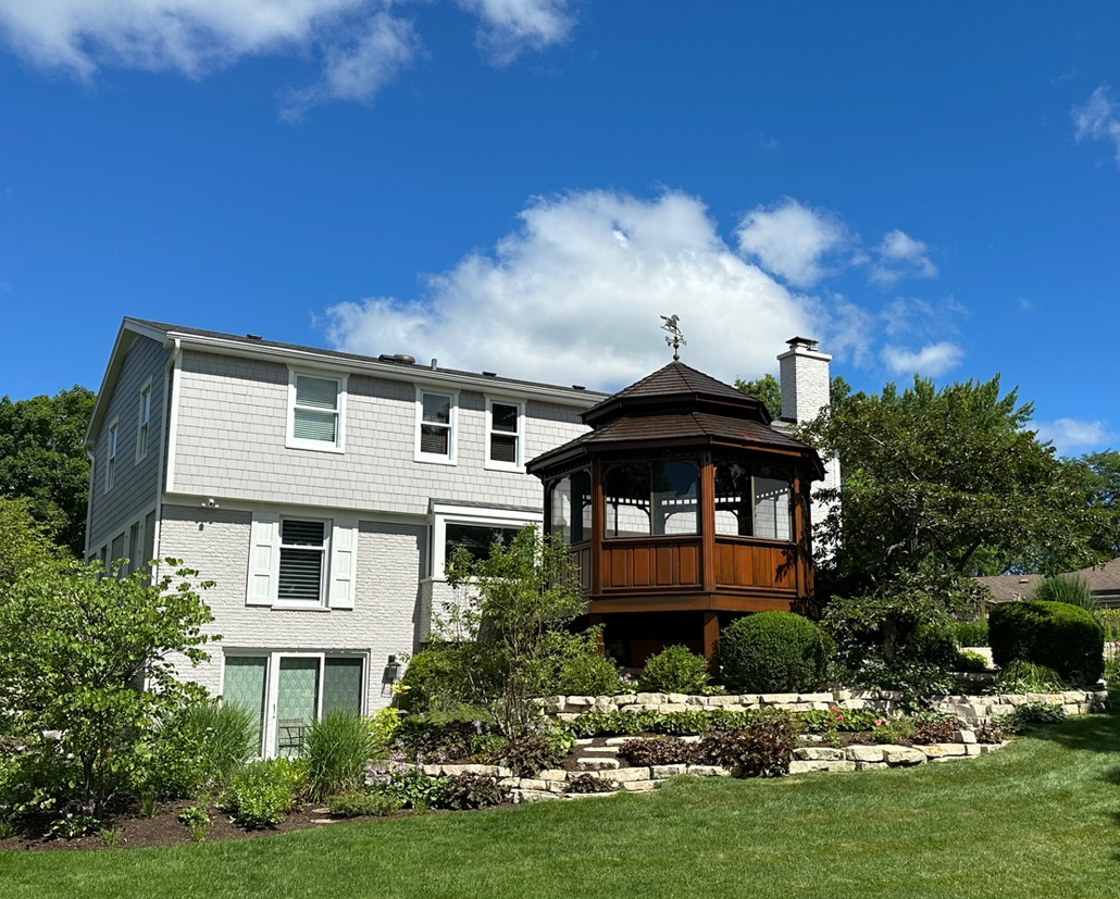 A large white house with a gazebo in the backyard on a sunny day.