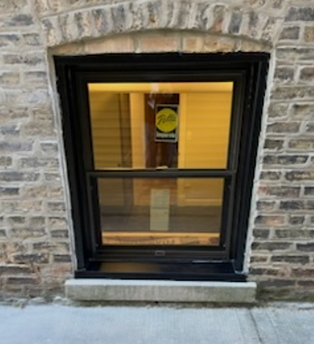 Black window with arched brick surround, set in brick wall; a concrete ledge at bottom.