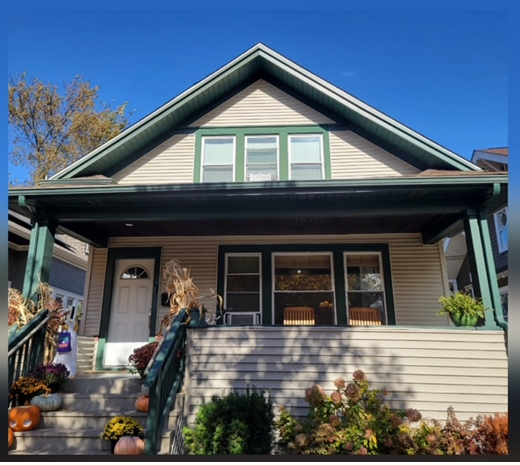 Pastel two-story house with green trim, porch, and pumpkins on steps, under a blue sky.