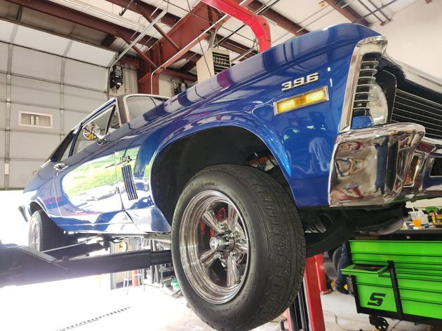 Blue classic car on a lift in an auto shop, with rear bodywork exposed and green equipment below