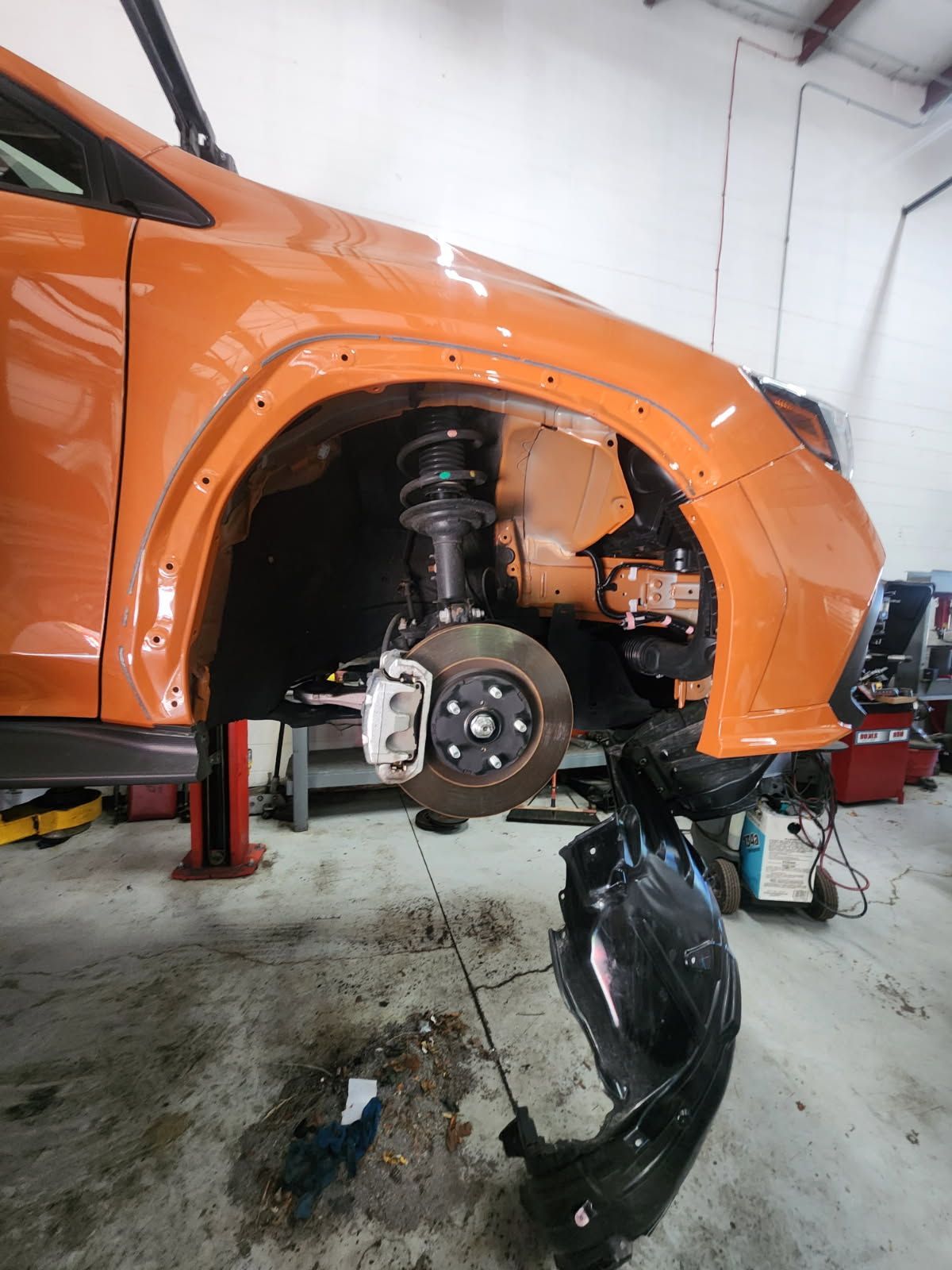 Orange car with front wheel removed in a garage, exposing the brake and suspension.