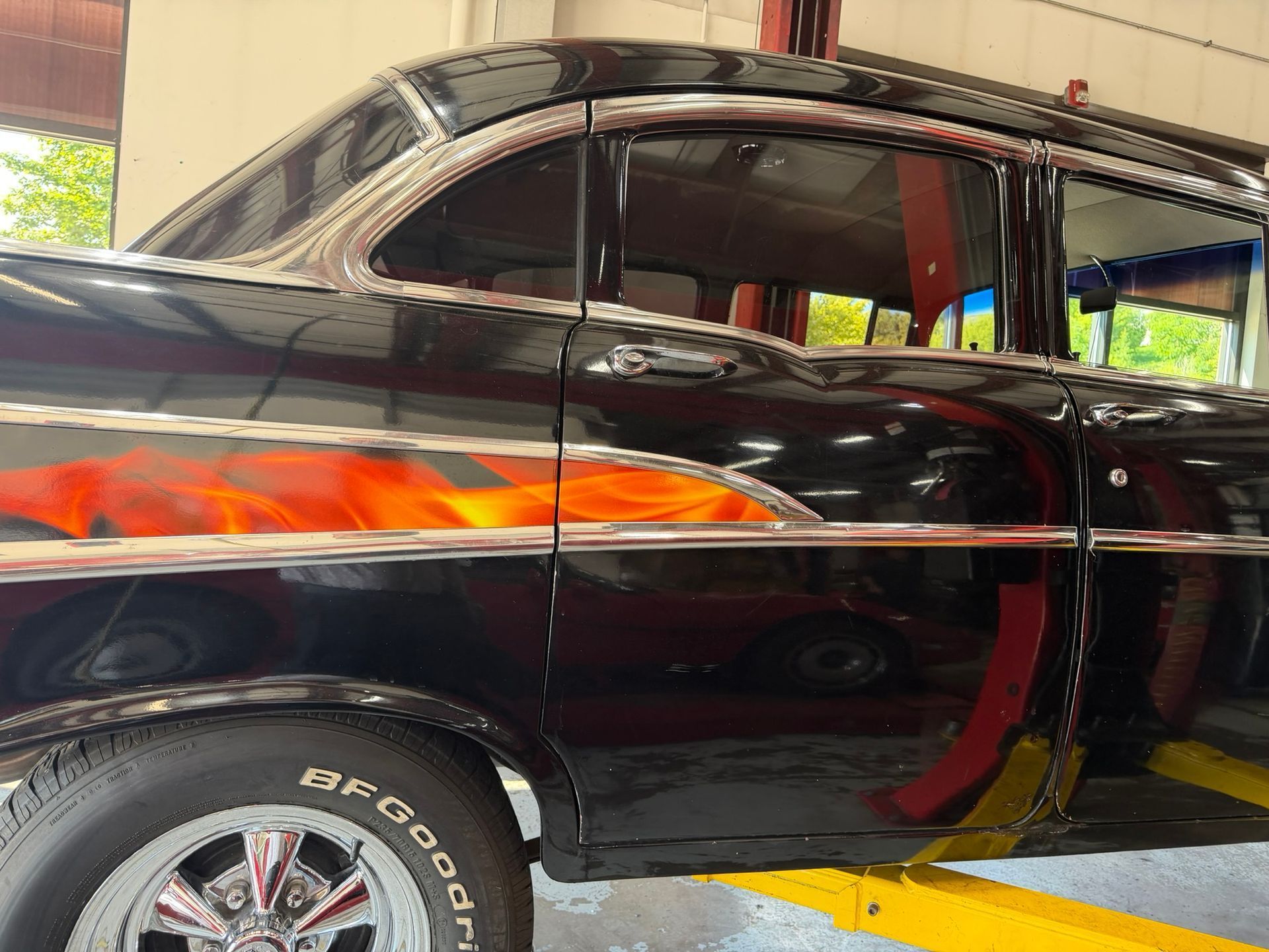 Black vintage car with orange flame decals, shown in a garage or showroom, side view