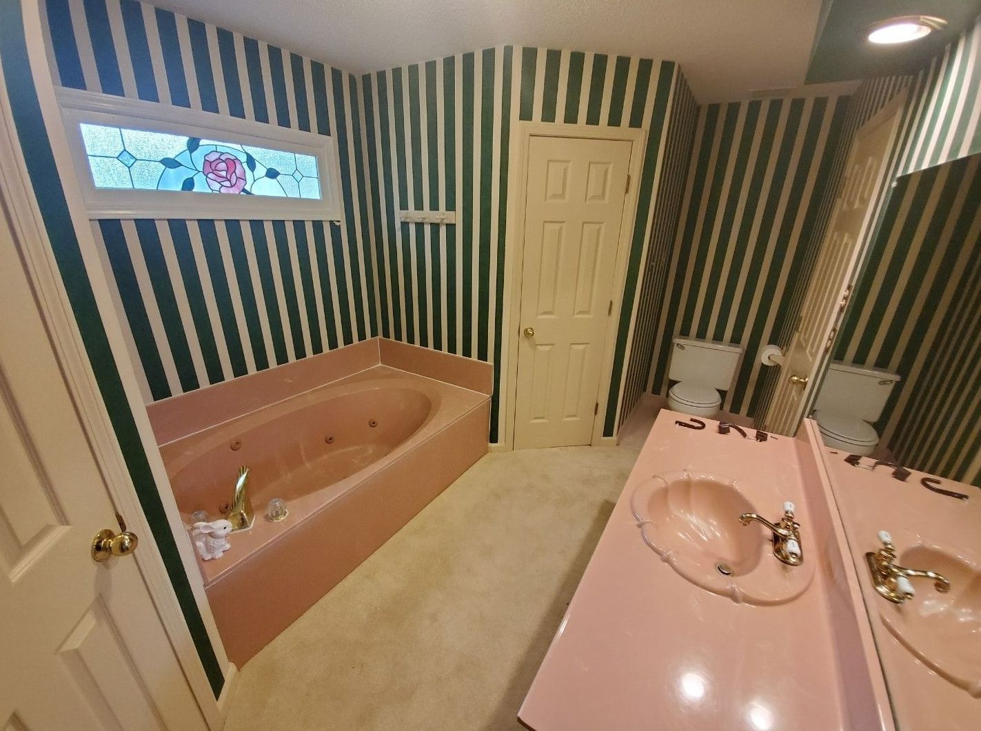 A bathroom with striped walls and a pink sink.