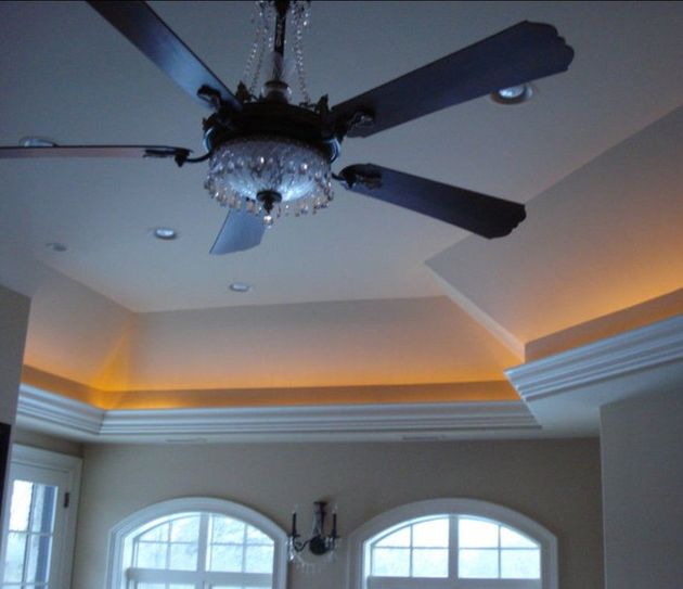 A ceiling fan with a crystal light fixture hangs in a room with a tray ceiling and warm perimeter accent lighting.