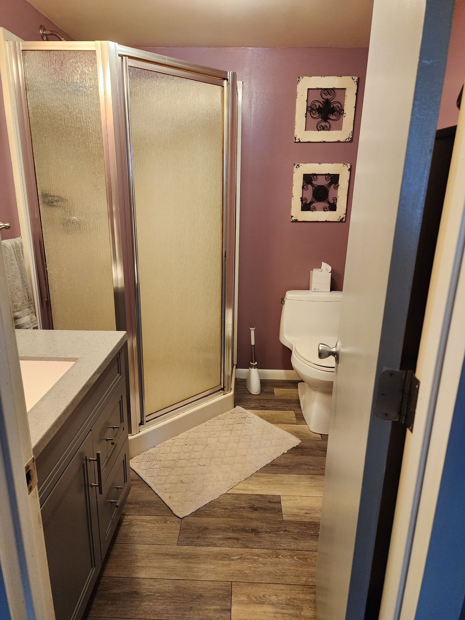 A bathroom with a toilet, sink, shower, and purple walls.