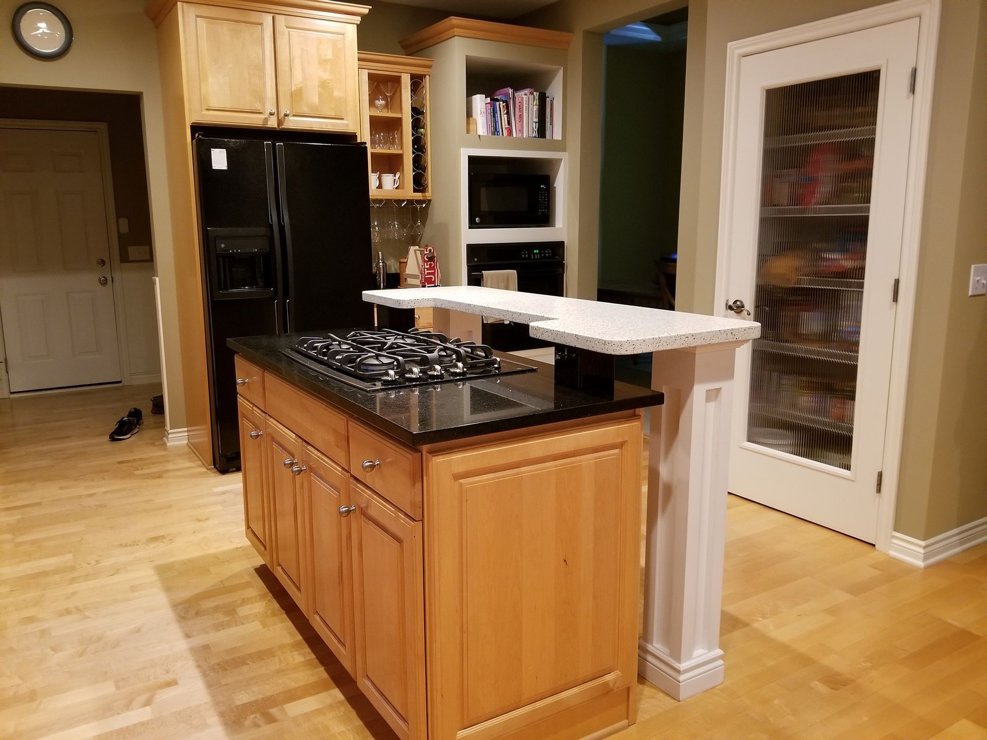 A kitchen with a large island with a stove top oven and a refrigerator.