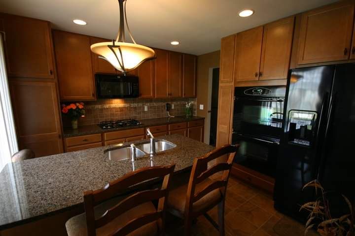 A kitchen with wooden cabinets , granite counter tops , a refrigerator , stove , sink and chairs.