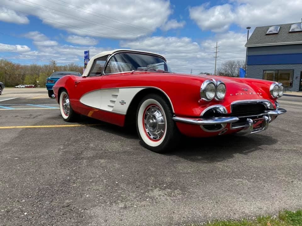 Red and white vintage Corvette convertible parked on asphalt on a sunny day.