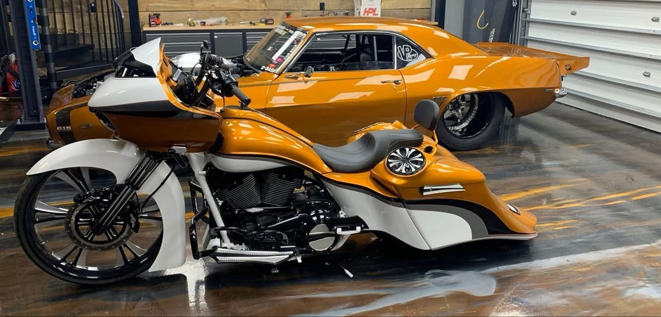 Motorcycle and classic muscle car in a garage. Both vehicles are orange and white.