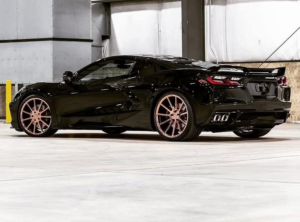 Black sports car with rose-gold wheels parked inside a building with yellow pillars.